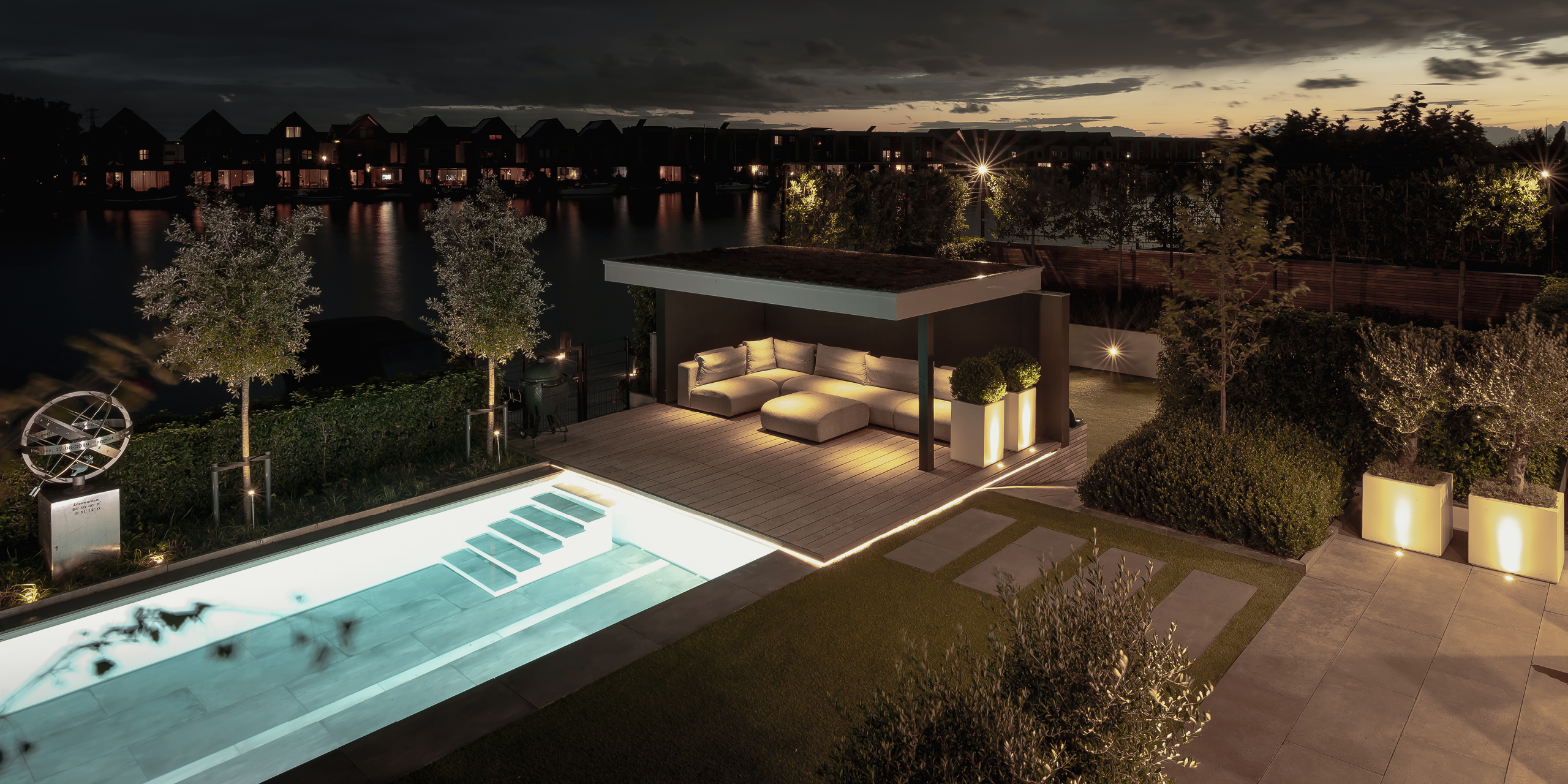 Buytengewoon wellnesstuin in Leeuwarden met zwembad, beplanting, steeneiken, tuinverlichting, terras, loungehoek en veranda.
