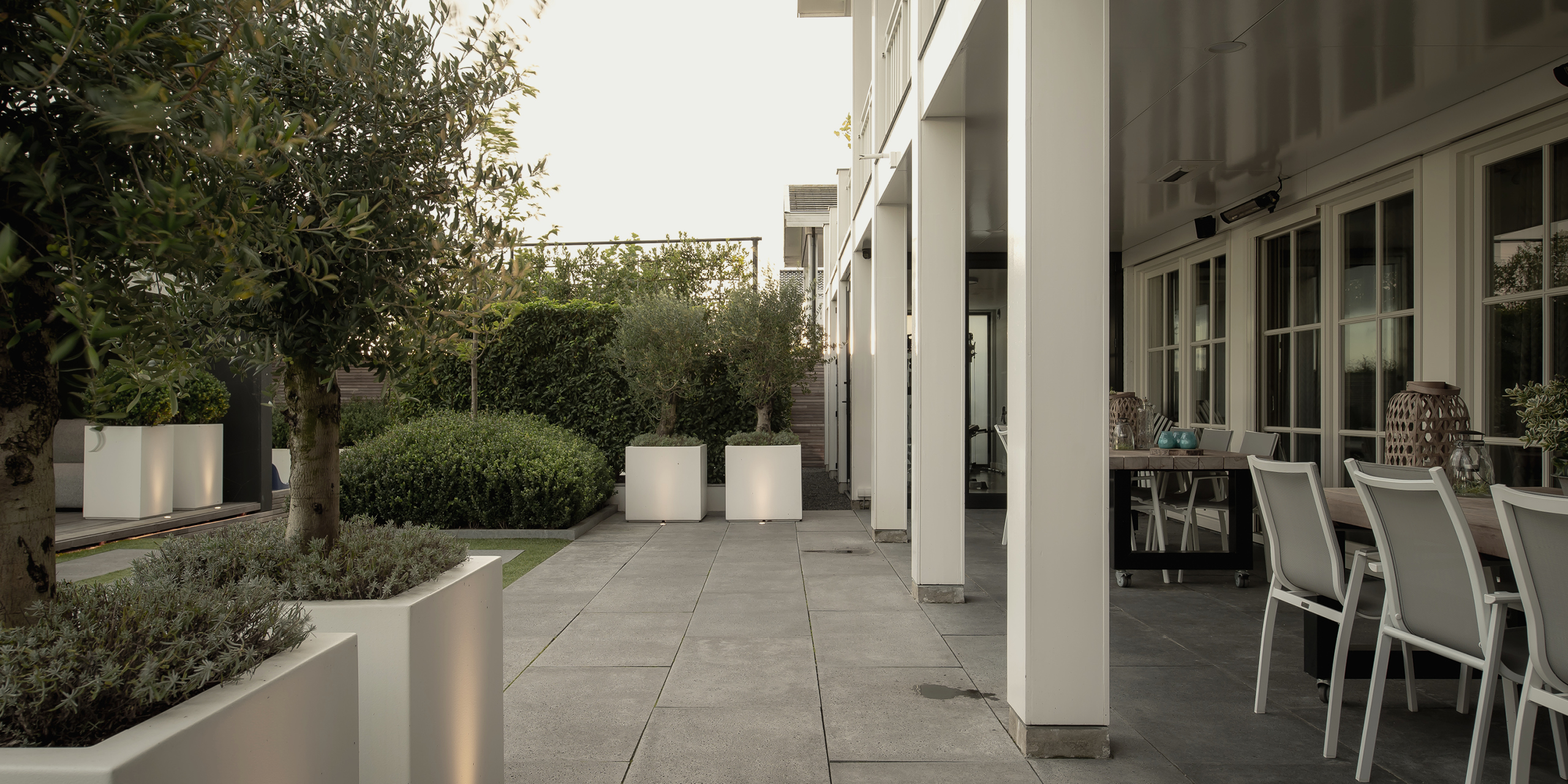 Buytengewoon wellnesstuin in Leeuwarden met terras, tuintafels, bloembakken en olijfbomen.