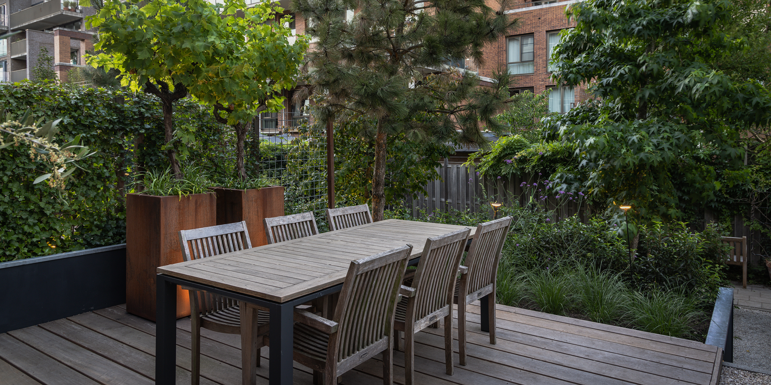 Amsterdamse Buytengewoon stadstuinen met druivenstruiken, tuintafel, vlonder, siergras en bomen.