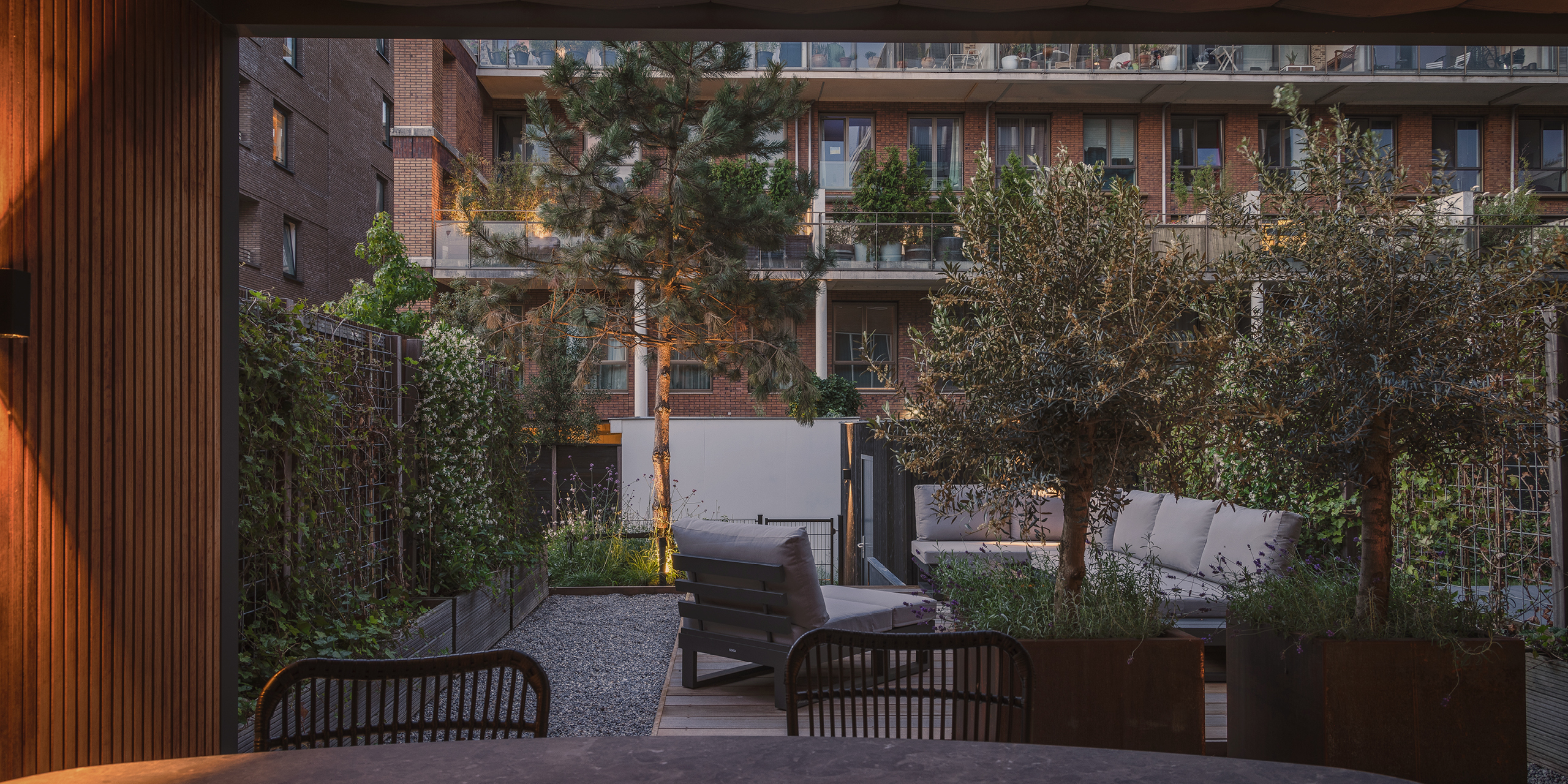 Amsterdamse Buytengewoon stadstuinen met olijfbomen, vliegden, loungehoek en tuintafel.
