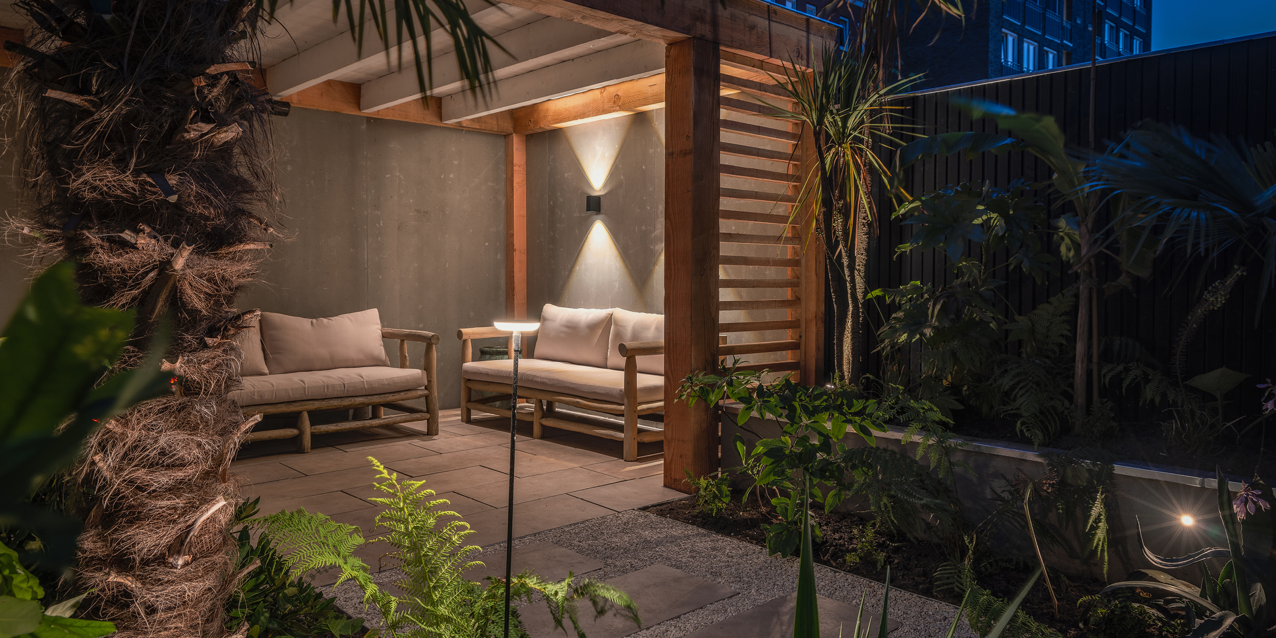 Amsterdamse Buytengewoon stadstuinen met tropische planten, veranda, zithoek, varens en buitenverlichting.