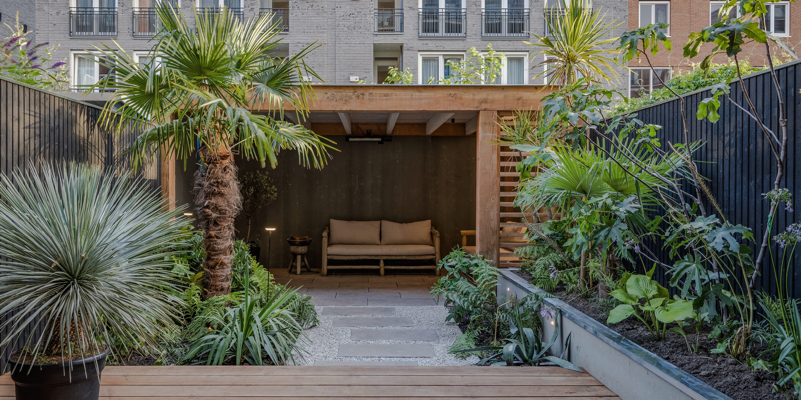 Amsterdamse Buytengewoon stadstuinen met veranda, zithoek, tropische planten en stapstenen.