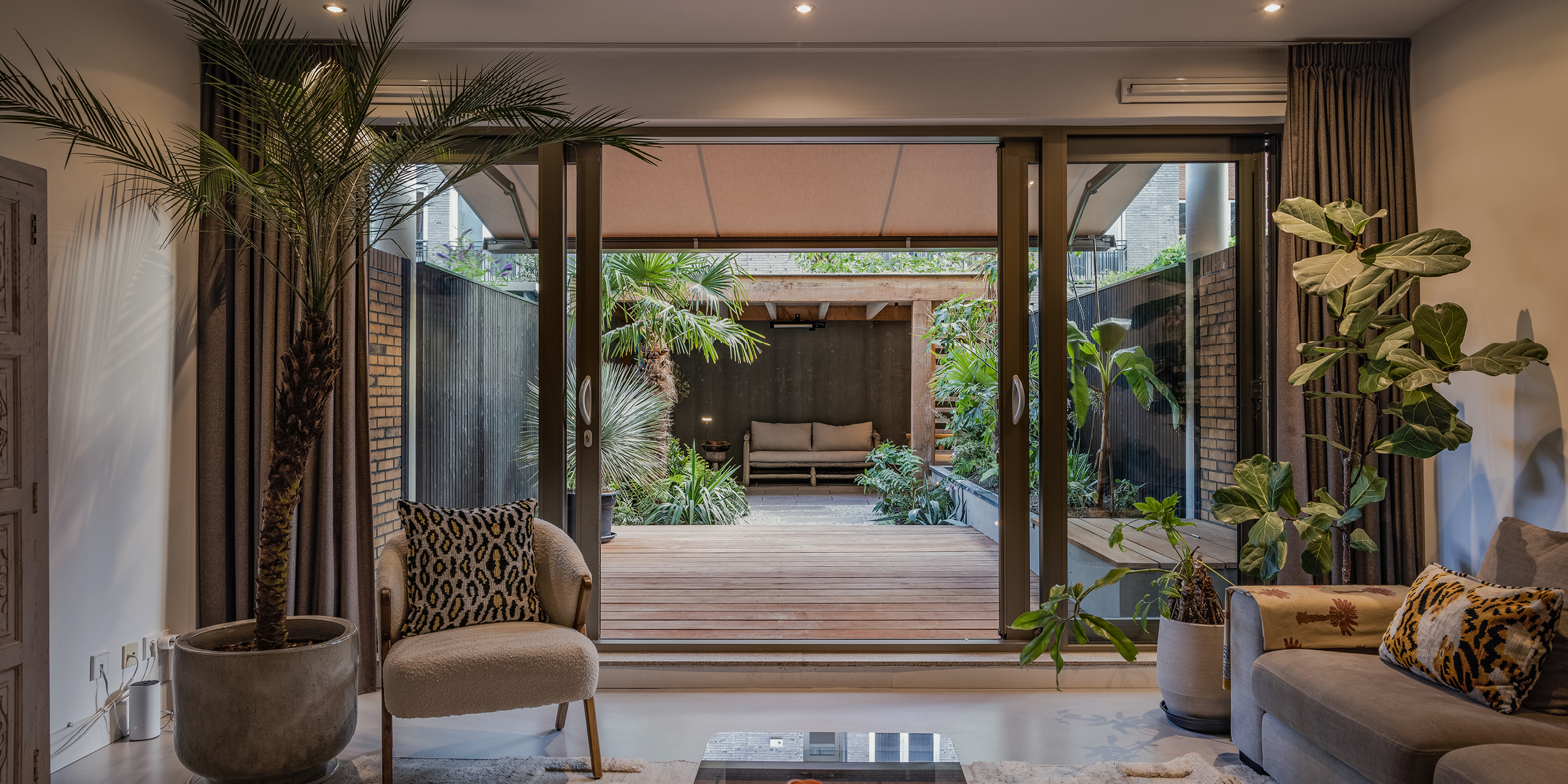 Amsterdamse Buytengewoon stadstuinen met vlonder, grind, tropische planten, veranda en loungehoek.