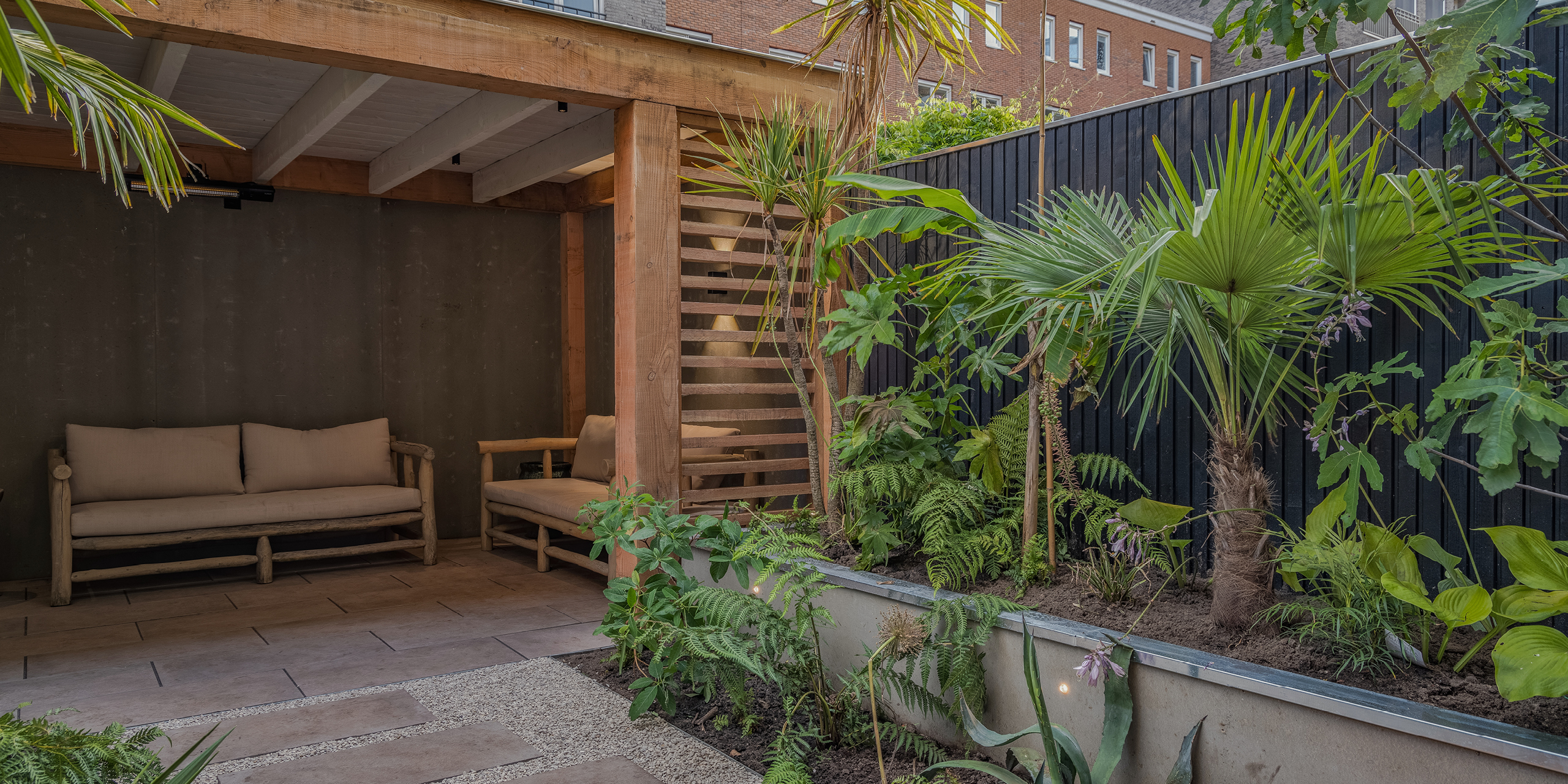 Amsterdamse Buytengewoon stadstuinen met veranda, verhoogd plantvak, tropische planten, varens en loungehoek.