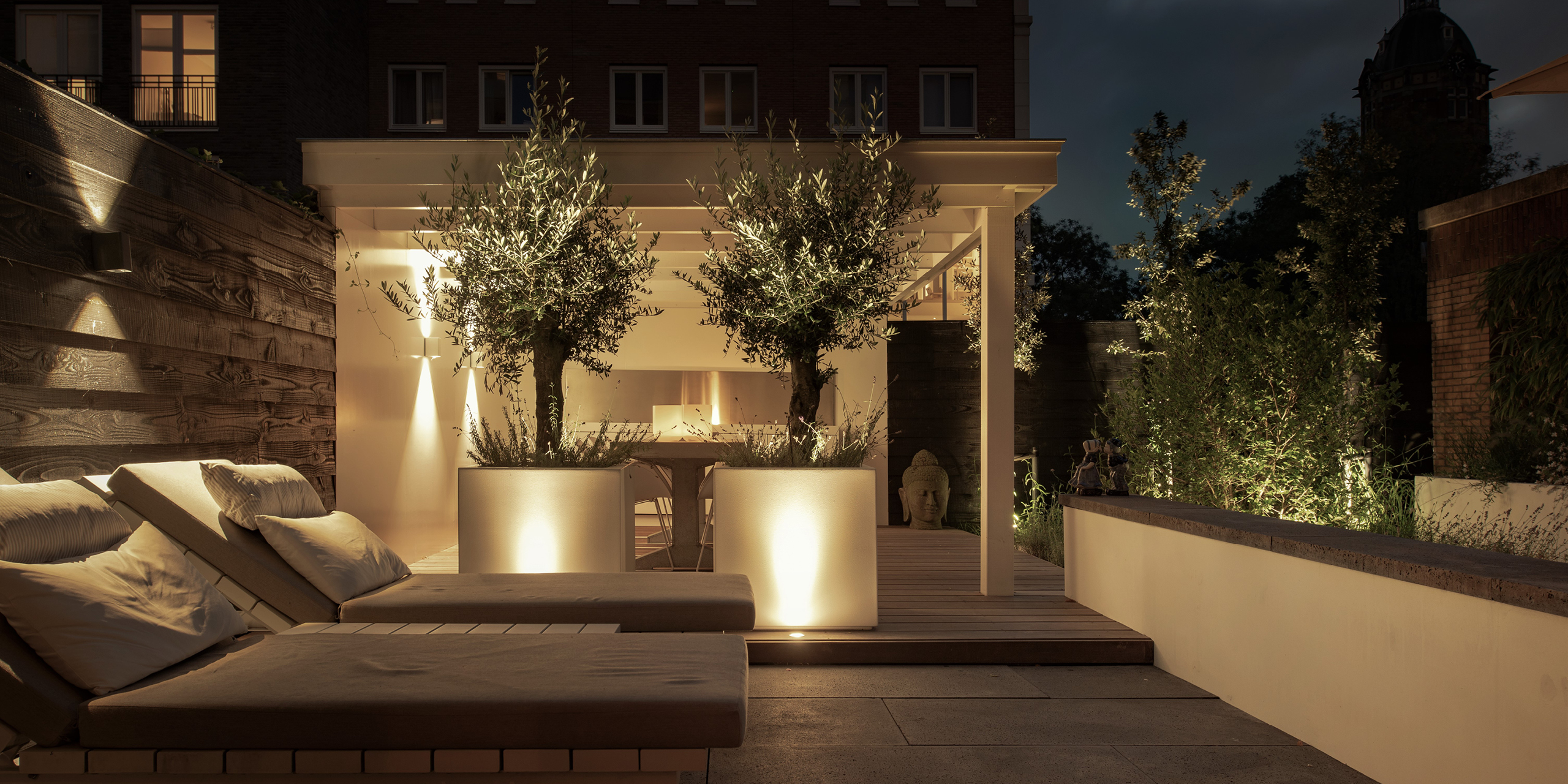 Patio van Buytengewoon in Amsterdam met ligbedden, olijfbomen en muurelement.